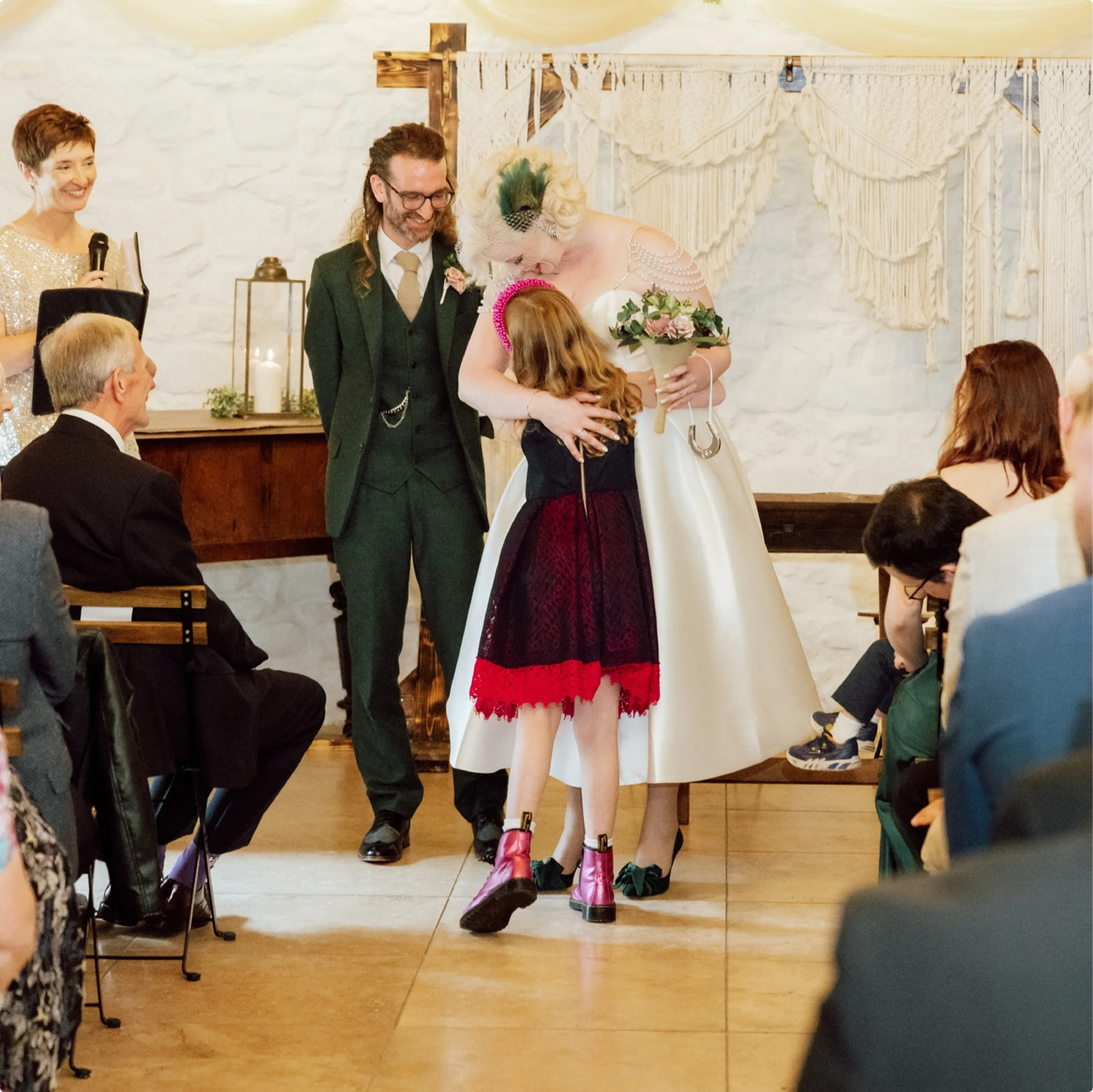 Bride hugging the flower girl during a wedding ceremony, with the groom beside them