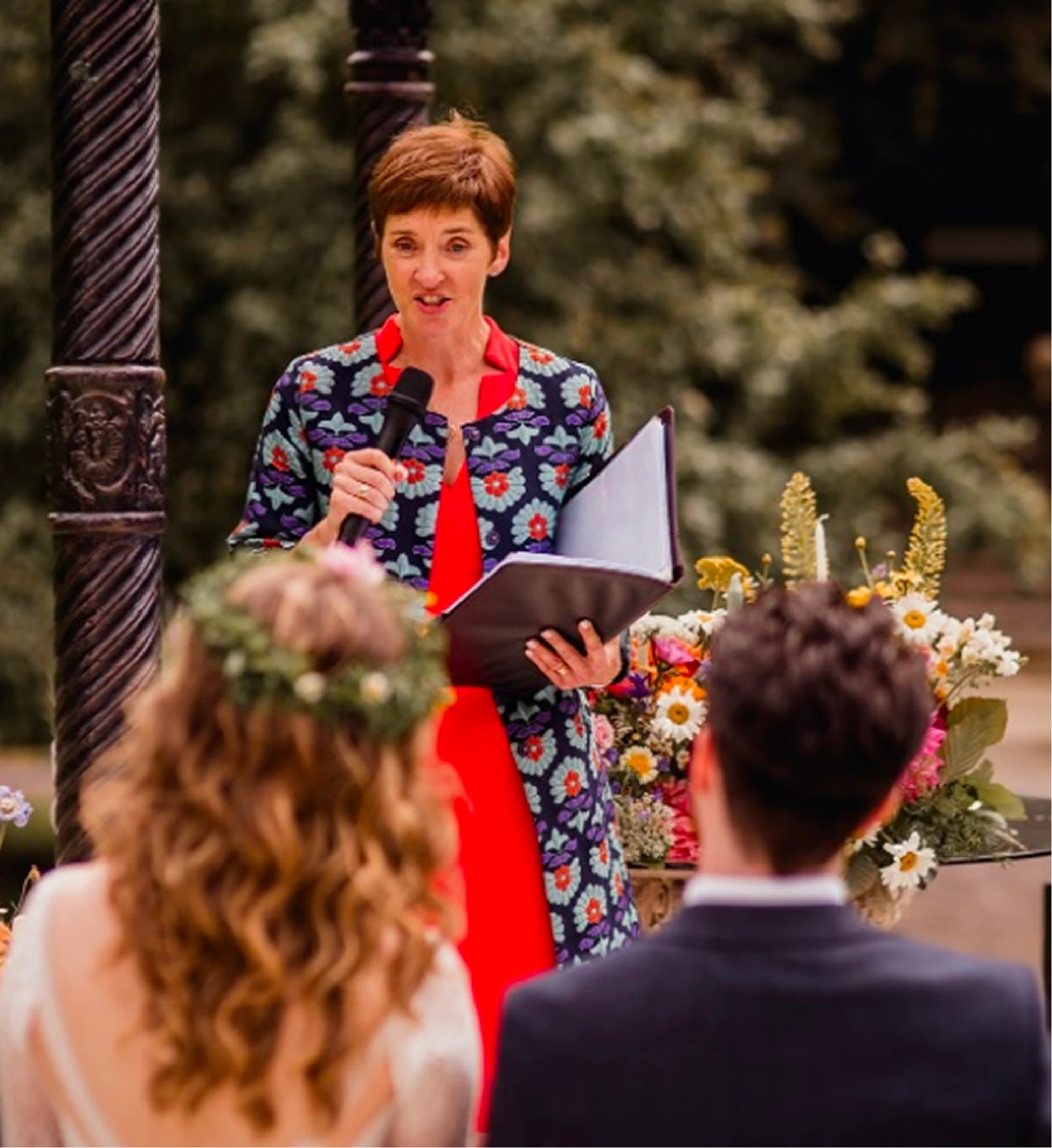Rosemary Hartigan reading at an outdoor wedding ceremony, the couple facing her