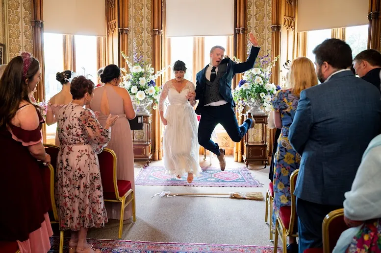 Laura and Mark jumping the broom at the end of their ceremony at Johnstown Castle, Wexford, guests applauding