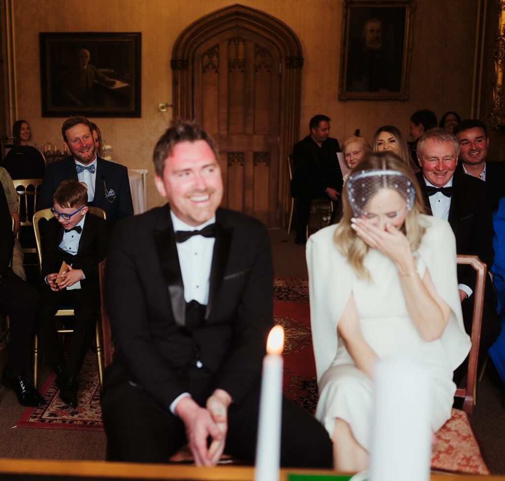 Maeve and Noel laughing during their wedding ceremony at Johnstown Castle, Wexford, with their guests behind them