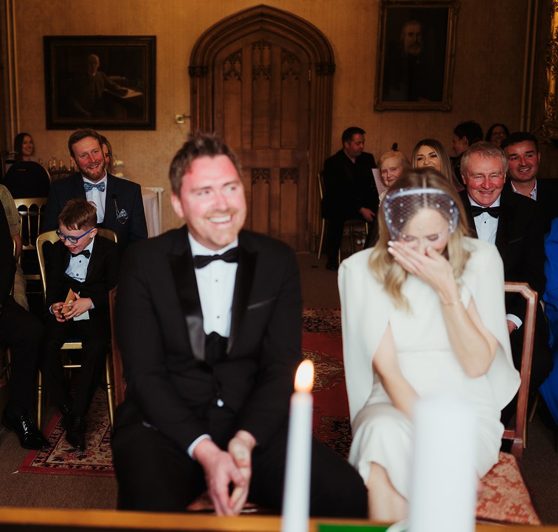 Maeve and Noel laughing during their wedding ceremony at Johnstown Castle, Wexford, with their guests behind them