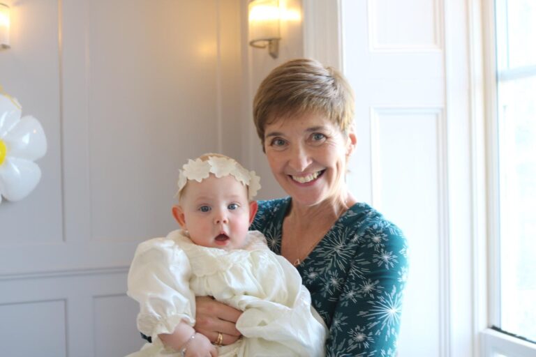 Celebrant Rosemary Hartigan smiling as she holds a baby in a christening gown during a family naming ceremony